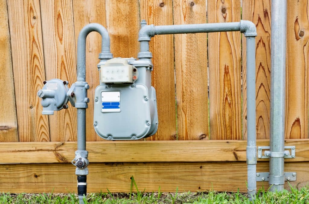 Natural gas meter in residential suburban backyard with wooden fence in background